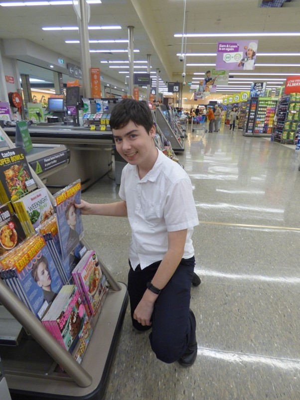 Lachlan kneeling down in a supermarket stacking magazines