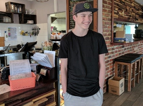 Kyal standing with his hands in his pockets, smiling and standing in a cafe